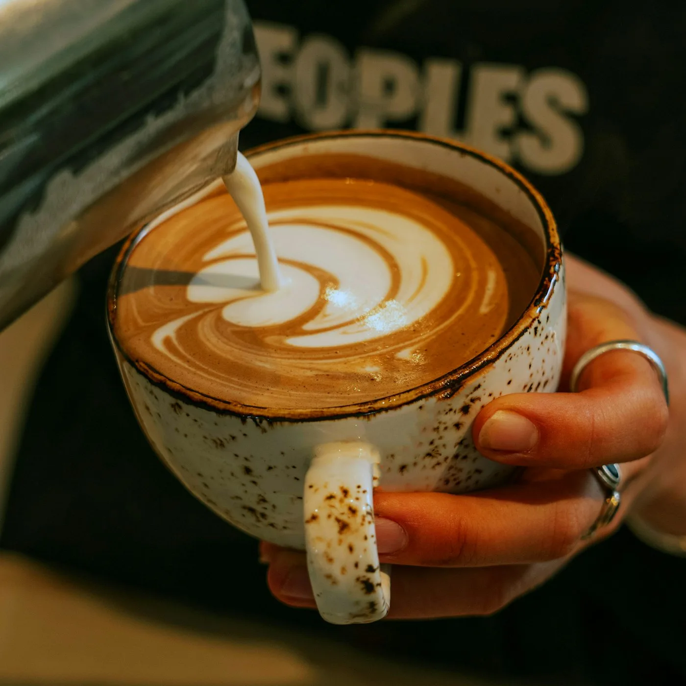 Milk being poured into a speckled mug to form latte art during a roastery course