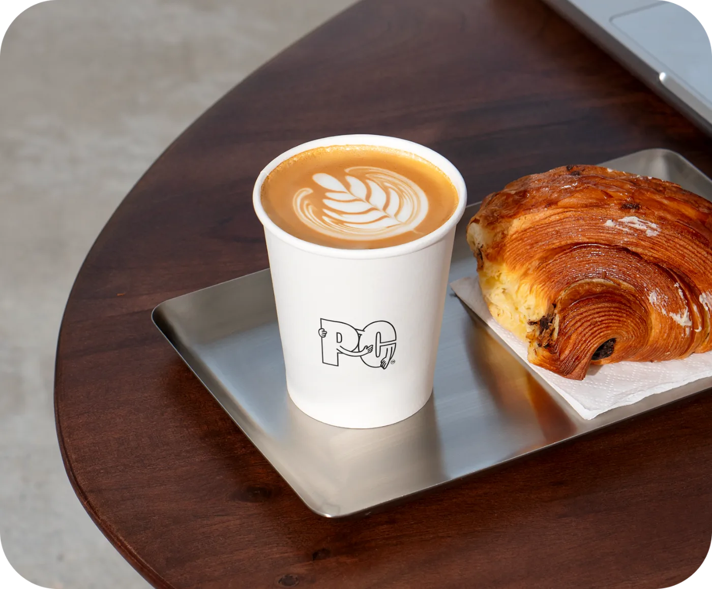 A Peoples Coffee flat white with latte art, served on a tray beside a pain au chocolat