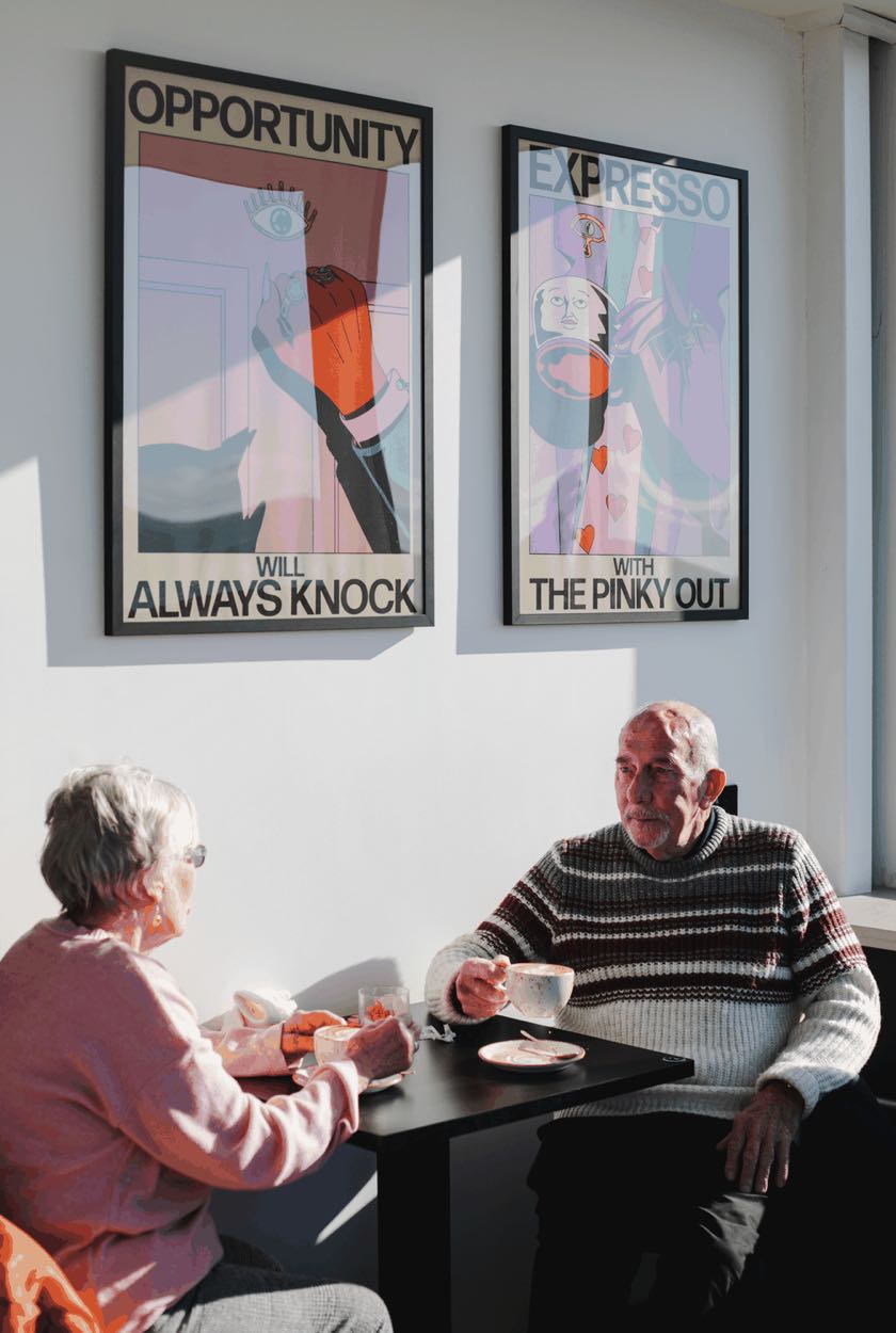 Two regulars chatting over coffee at a window table in the Peoples Coffee cafe